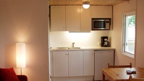 Kompakti keittiö, jossa on mikroaaltouuni, kahvinkeitin ja astianpesukone. Viereisessä olohuoneessa on ruokapöytä tuoleineen ja punainen sohva.