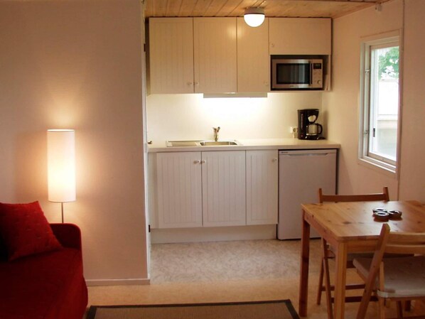 A compact kitchen with a microwave, coffee maker, and dishwasher. There is a dining table with chairs and a red sofa in the adjacent living area. - 2 Person Holiday Home in Tyringe (Tyringe)