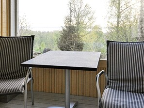 Un pequeño espacio al aire libre con dos sillas a rayas y una mesa cuadrada, con vistas a un paisaje boscoso.