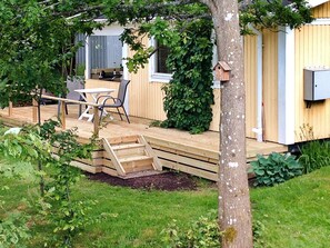 Una terraza de madera con mesa y sillas, un comedero para pájaros y un pequeño jardín.