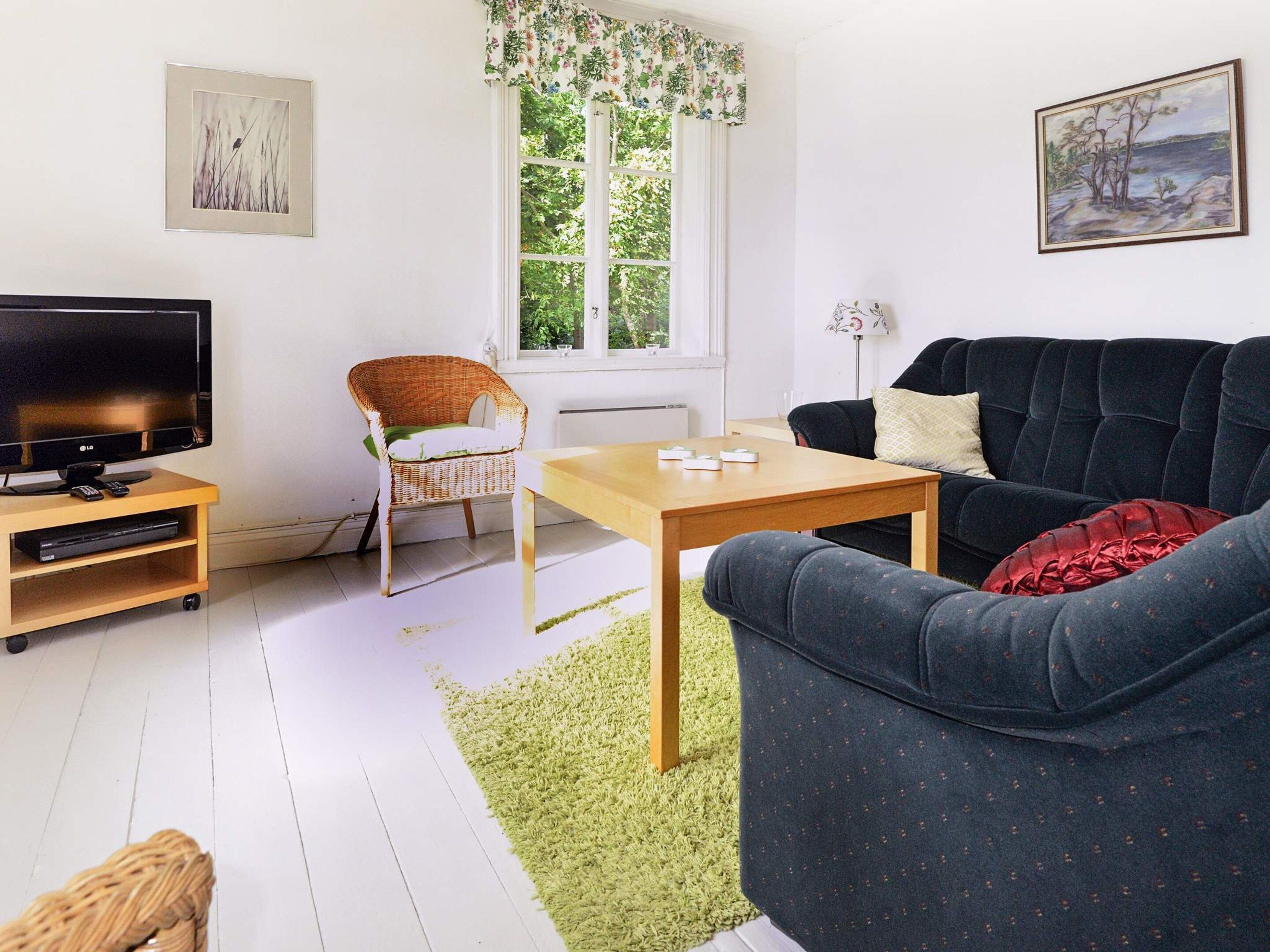A living room with a television, a wicker chair, a sofa, a coffee table, and artwork on the walls.