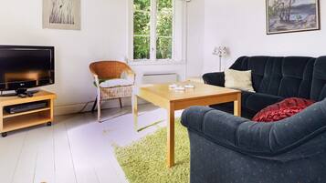 A living room with a television, a wicker chair, a sofa, a coffee table, and artwork on the walls.