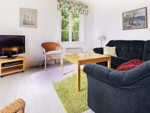A living room with a television, a wicker chair, a sofa, a coffee table, and artwork on the walls.