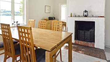 Uma sala de jantar com mesa e cadeiras de madeira, lareira e vista através de grandes janelas.