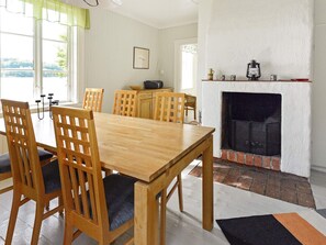 A dining area with a wooden table and chairs, a fireplace, and a view through large windows. - 5 Person Holiday Home in Mariefred (Mariefred)