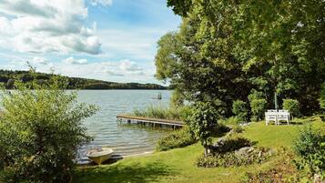 Un entorno junto al lago con un muelle, un bote y una mesa de picnic.