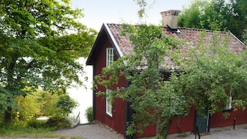 A red house with a sloped roof, surrounded by greenery and a gravel path.
