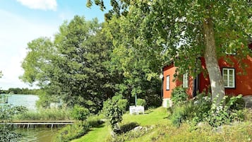 A red building with a white door, surrounded by lush greenery and a body of water.