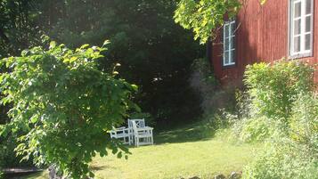 A red building with a window, surrounded by greenery and a stone wall.