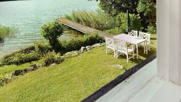 A lakeside view with a wooden dock, a white table and chairs, and a grassy area.