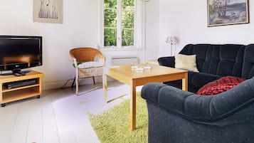 Ett vardagsrum med en tv, en fåtölj i rotting, en soffa, ett soffbord och konstverk på väggarna.