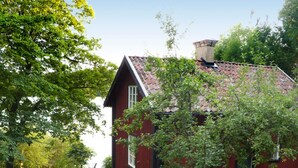 A red house with a sloped roof, surrounded by greenery and a gravel path. - 5 Person Holiday Home in Mariefred (Mariefred)