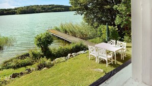 A lakeside view with a wooden dock, a white table and chairs, and a grassy area. - 5 Person Holiday Home in Mariefred (Mariefred)
