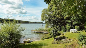 Un paisaje junto al lago con un muelle, un bote y una mesa de picnic.