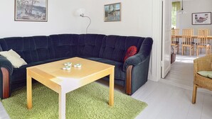 A living room with a dark blue sofa, a wooden coffee table, and a green area rug. There are two framed artworks on the wall and a dining area with wooden chairs and a table. - 5 Person Holiday Home in Mariefred (Mariefred)