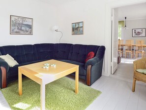 A living room with a dark blue sofa, a wooden coffee table, and a green area rug. There are two framed artworks on the wall and a dining area with wooden chairs and a table. - 5 Person Holiday Home in Mariefred (Mariefred)