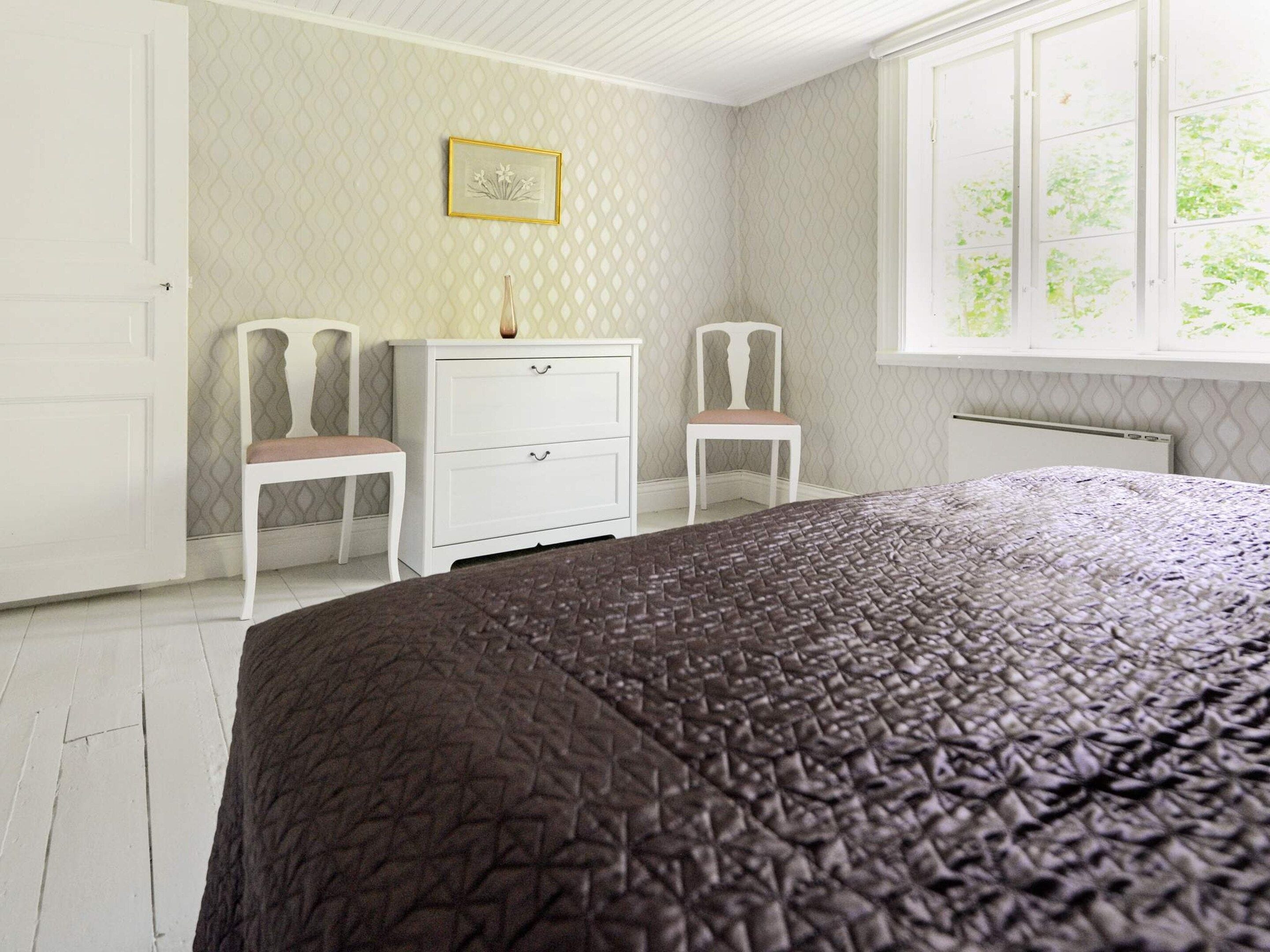 A bedroom with a bed, two chairs, a dresser, and a window with a view.