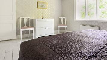 A bedroom with a bed, two chairs, a dresser, and a window with a view.