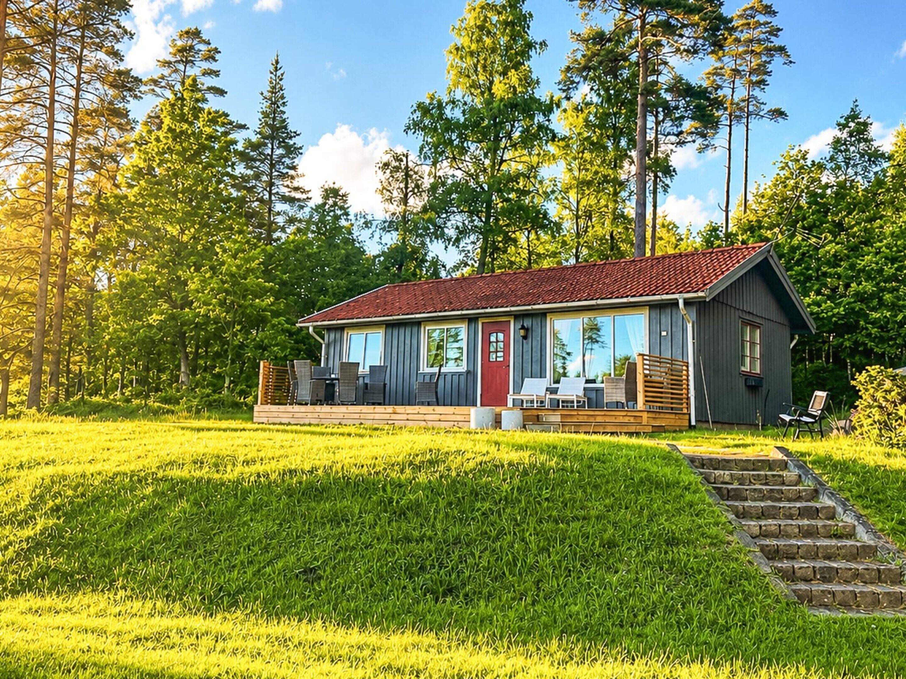 A cabin with a red roof, large windows, and a deck with outdoor seating.