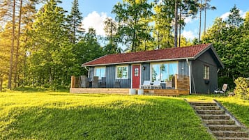 A cabin with a red roof, large windows, and a deck with outdoor seating.