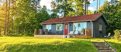 A cabin with a red roof, large windows, and a deck with outdoor seating.