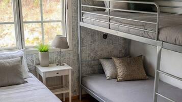 A bunk bed room with a window, a bedside table with a lamp, and a small plant.