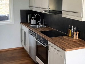 A modern kitchen with stainless steel appliances, a wooden countertop, and a black backsplash. - Holiday Home in HÃ¥cksvik (Håcksvik)