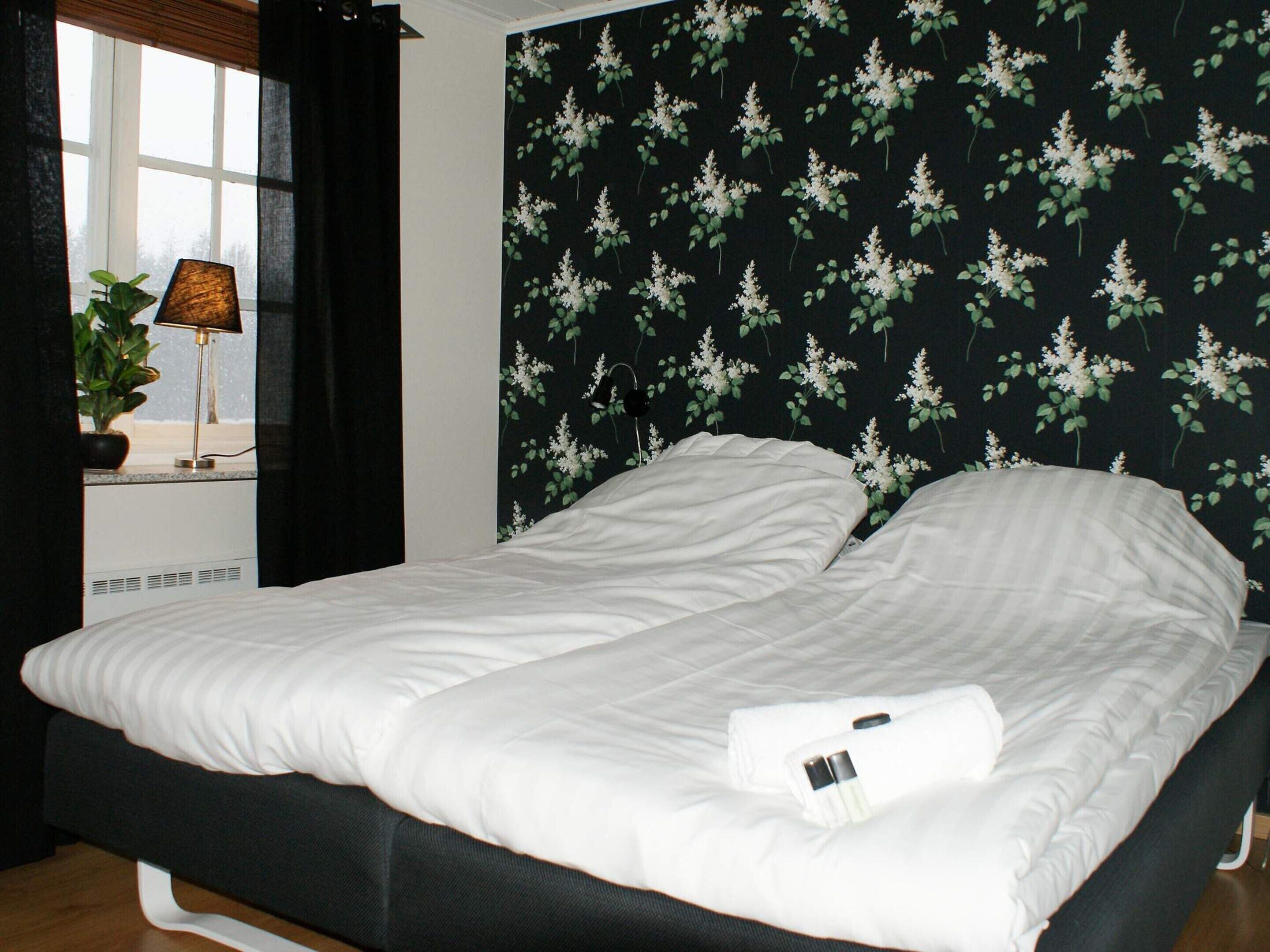 A bed with white bedding, a dark headboard, and a window with a view of the outdoors.