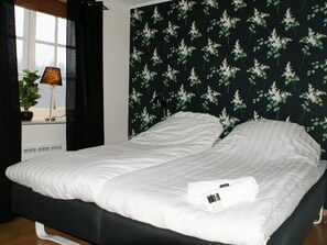 Una cama con ropa blanca, cabecera oscura y ventana con vistas al exterior.