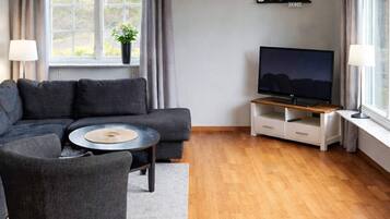 A modern living room with a sectional sofa, a coffee table, a TV on a wooden stand, and a window with curtains.