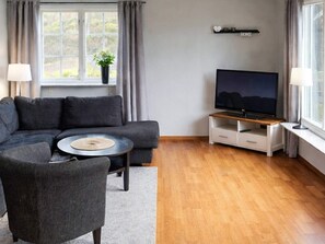 Una sala de estar moderna con un sofá modular, una mesa de centro, un televisor sobre un mueble de madera y una ventana con cortinas.