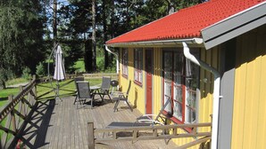 A wooden deck with outdoor furniture and a grill, leading to a yellow building with a red roof. - Holiday Home in HÃ¥cksvik (Håcksvik)