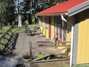 A wooden deck with outdoor furniture and a grill, leading to a yellow building with a red roof. - Holiday Home in HÃ¥cksvik (Håcksvik)