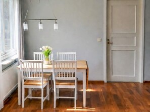 Un comedor con mesa de madera y sillas blancas, un florero con flores y una lámpara colgante.