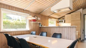 A modern interior with a dining table, chairs, a kitchen area, and a window with a view of greenery. - 4 Star Holiday Home in Stege (Stege)