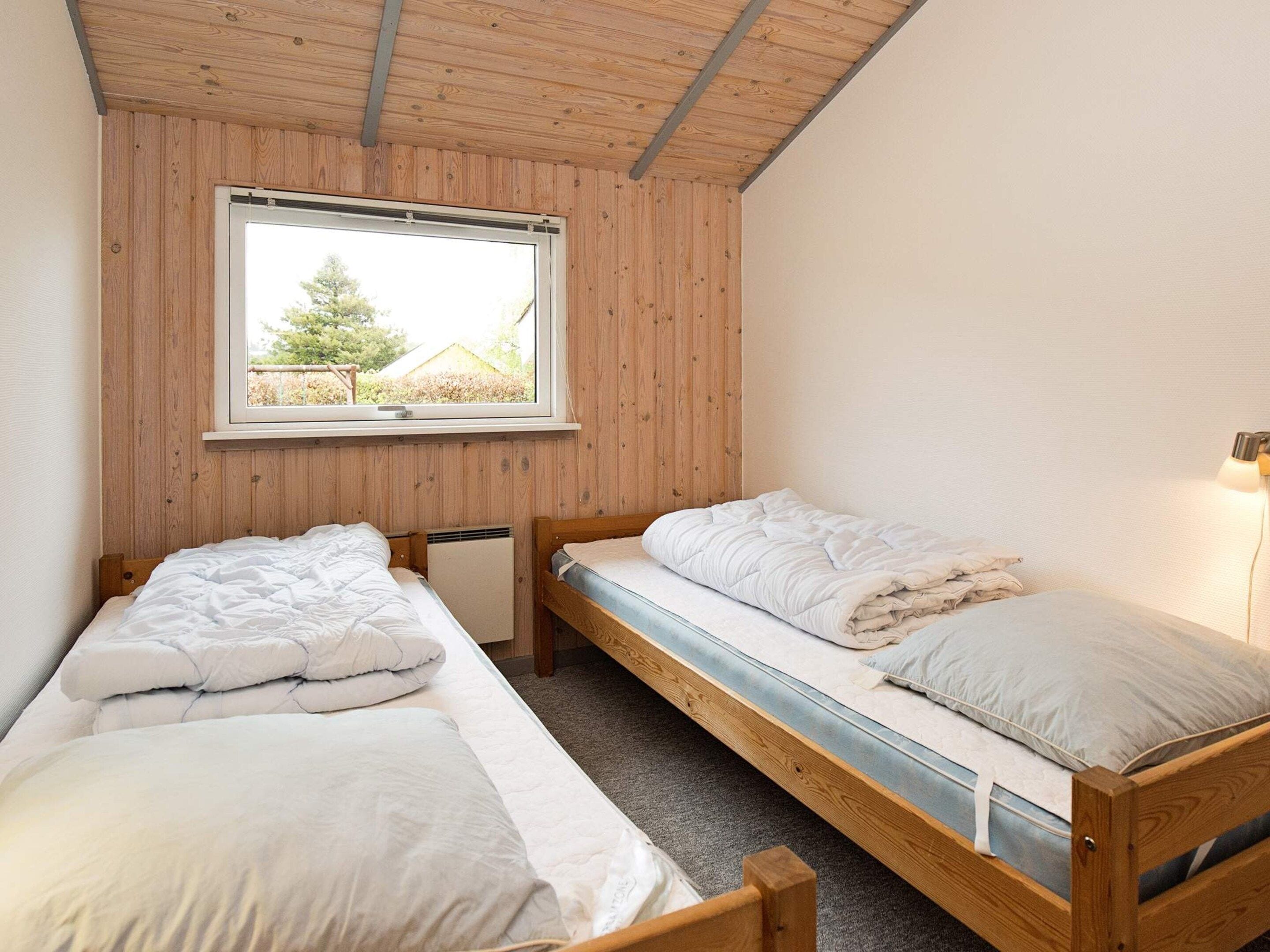 Una habitación con dos literas de madera, una ventana que da a vistas de vegetación y un calentador fijado a la pared.