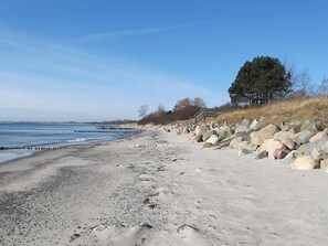 Une plage de sable avec de gros rochers, un escalier en bois et un arbre.