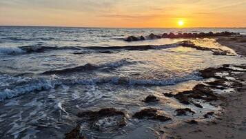 Una playa con olas, rocas y una puesta de sol.