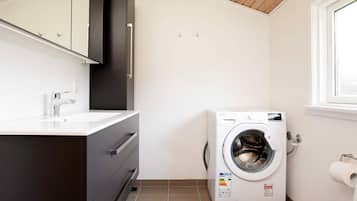 A compact laundry room with a washing machine, a sink, and a mirror above the cabinet.