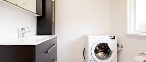 A compact laundry room with a washing machine, a sink, and a mirror above the cabinet.