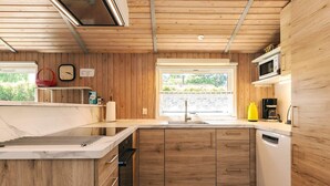 A modern kitchen with wooden cabinets, a built-in dishwasher, and a window with a view of greenery. - 4 Star Holiday Home in Stege (Stege)