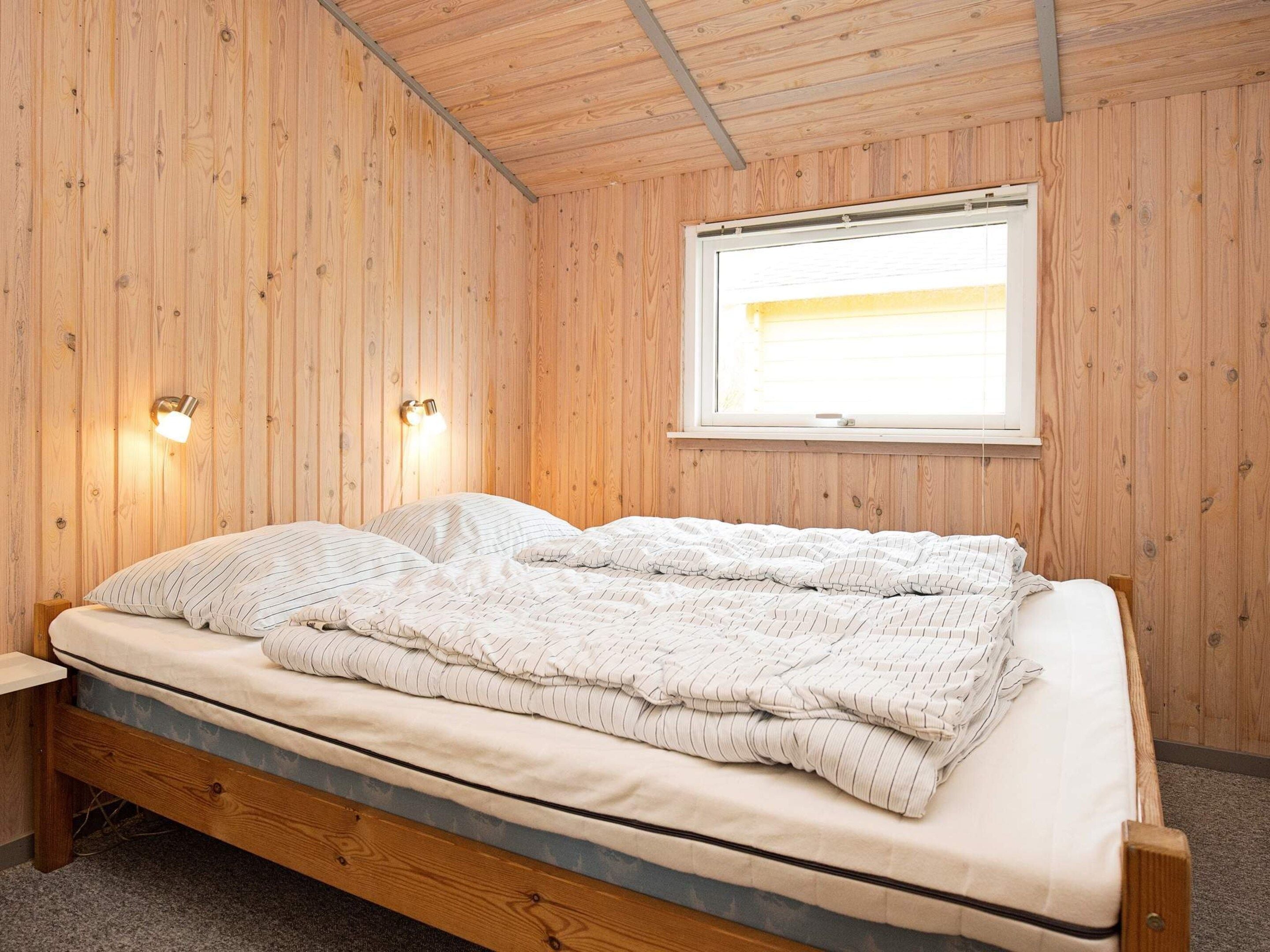 A wooden-paneled room with a bed, two wall-mounted lights, and a window.