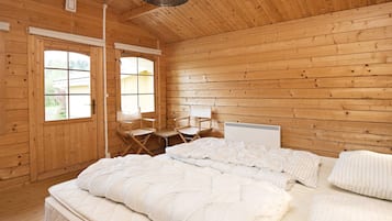 A wooden cabin room with a bed, two chairs, a window, and a ceiling light.