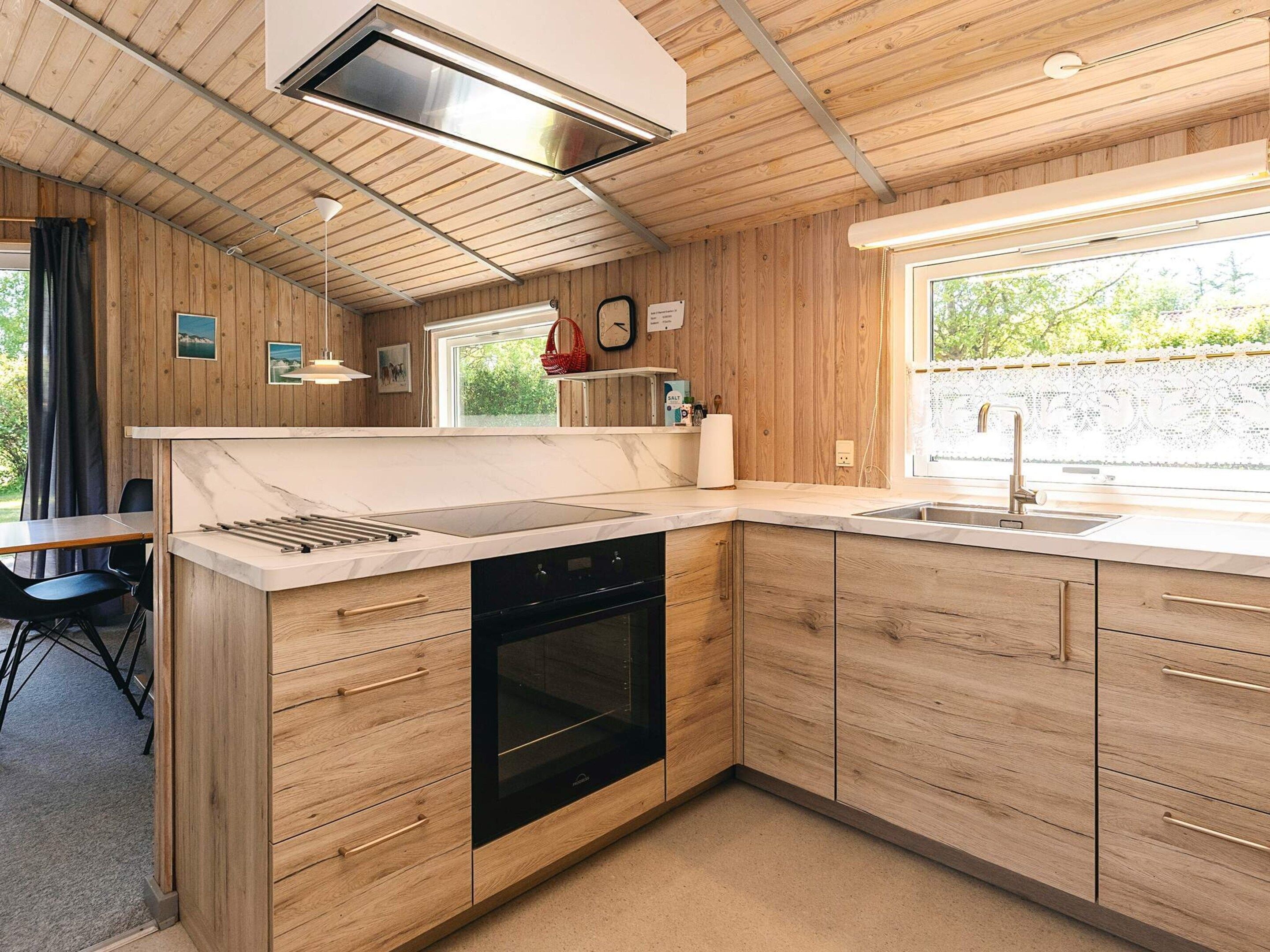 A modern kitchen with wooden cabinetry, a built-in oven, and a large window providing natural light.