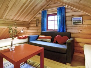 Ein gemütliches Cabin-Interieur mit Holzbalkendecke, einer Couch mit Kissen, einem kleinen Tisch und einem Fenster mit Vorhängen.