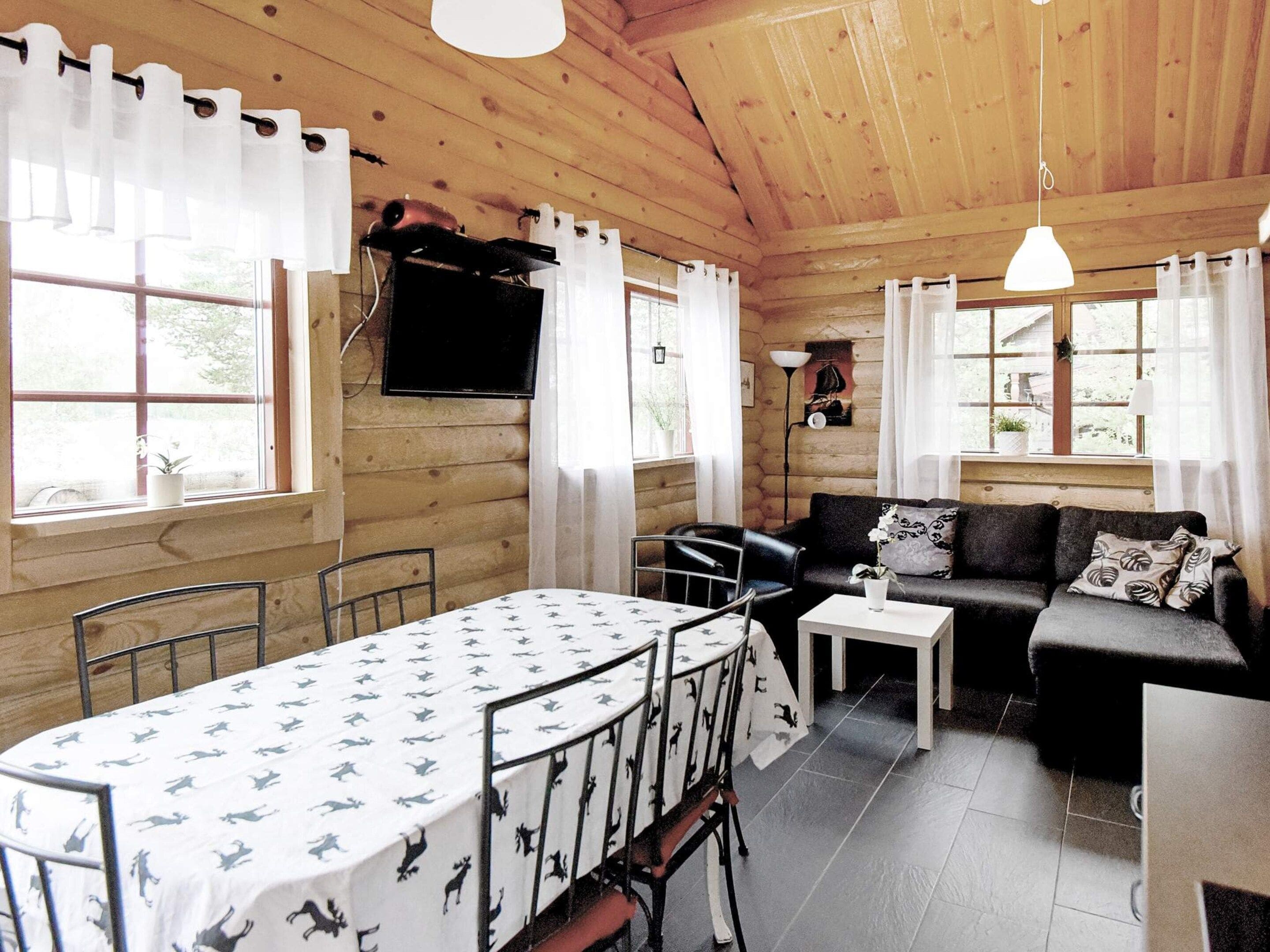 Interior acogedor de una cabaña con una mesa de comedor, sillas, un sofá y un televisor montado en la pared.