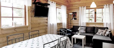 A cozy cabin interior with a dining table, chairs, a sofa, and a television mounted on the wall.