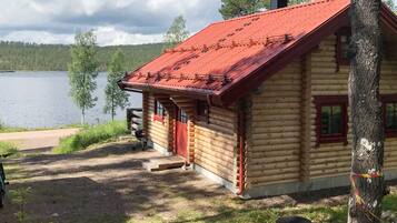 Una cabaña de troncos con techo rojo, ubicada junto a un lago con vistas claras al agua.