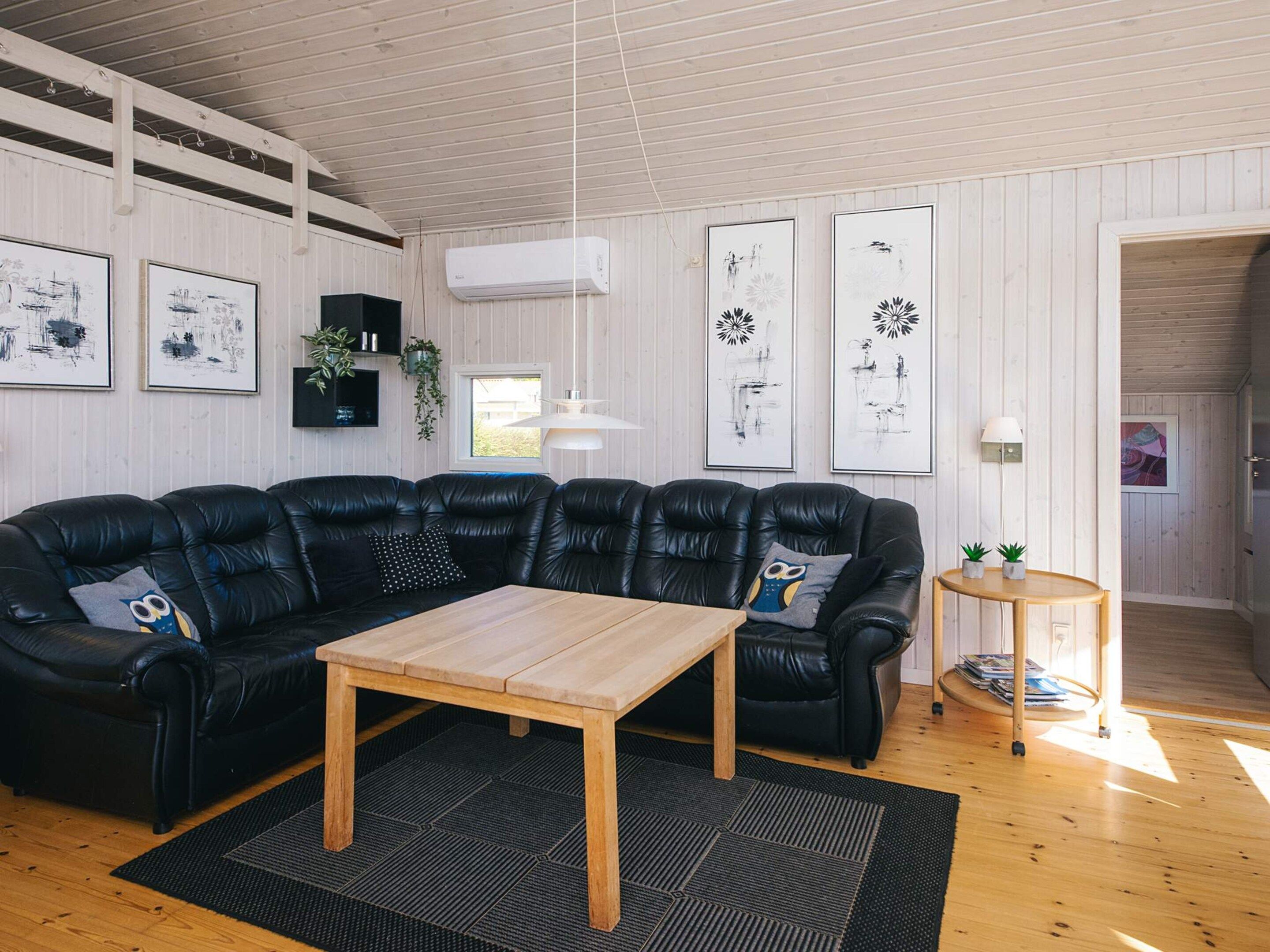 Una sala de estar moderna con un sofá seccional de cuero negro, una mesa de centro de madera y una alfombra negra y gris.