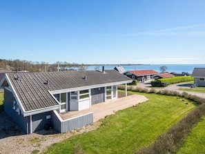 Uma casa moderna com telhado inclinado, varanda coberta e vista para o mar.